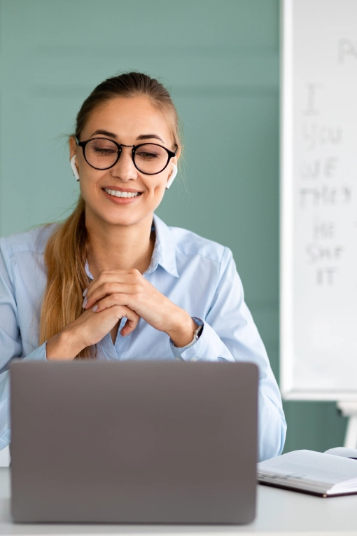 Woman wearing glasses and earbuds participating in an online meeting while using a laptop